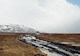 Permafrost field and unmaintained road with snow covered mountain in background