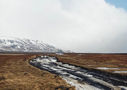 Permafrost field and unmaintained road with snow covered mountain in background