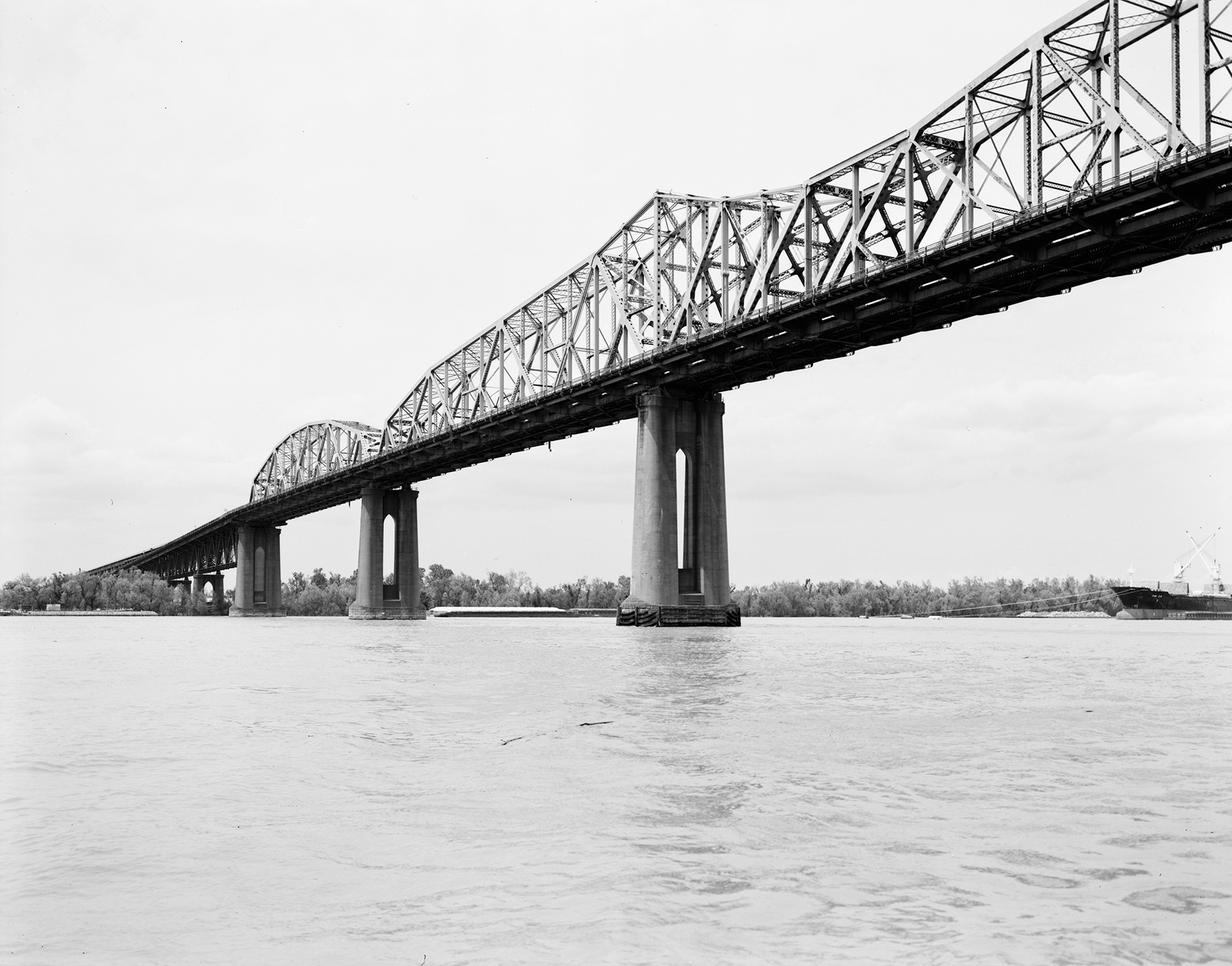 Photo shows a steel bridge with concrete piers. The bridge spans a river. 
