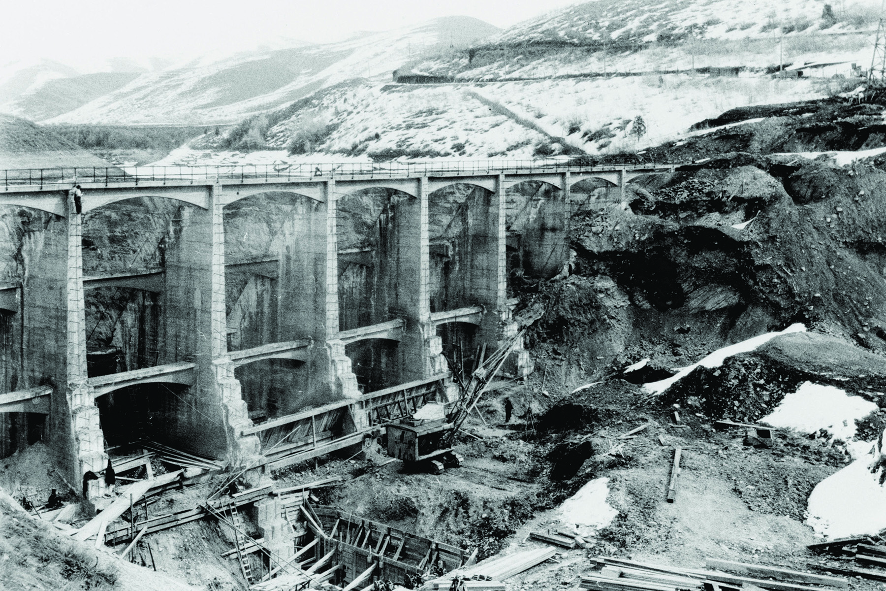 Photocopy of a photograph shows men adding height to a concrete dam. 