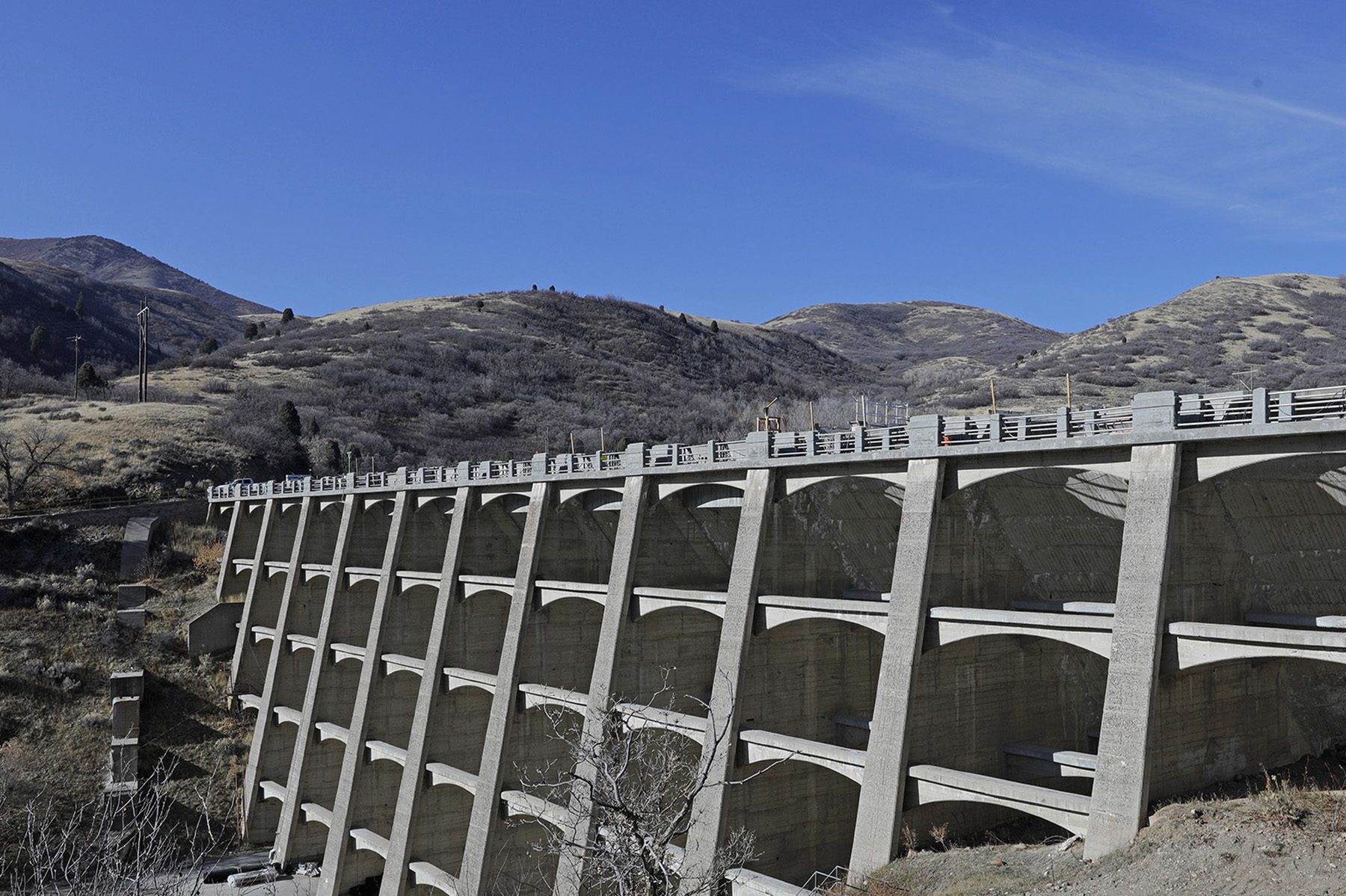 Photograph shows a multiple-arch dam set amidst trees and hills. 