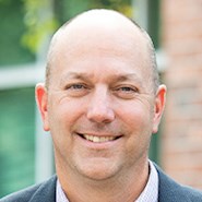 Man in jacket and tie smiles at the camera.