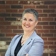 Woman wearing gray blazer with short hair smiles at the camera.