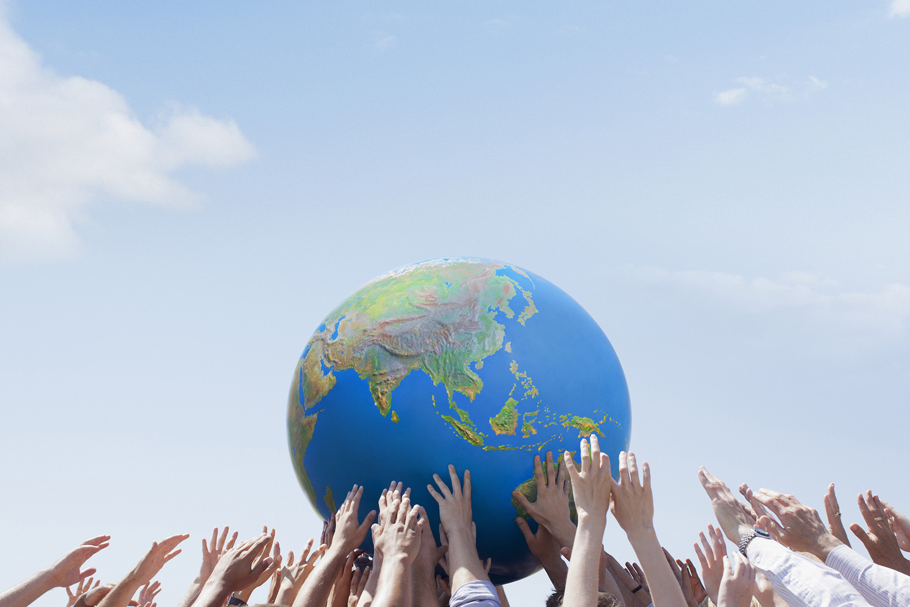 Hands hold up a ball that has the continents on it. 