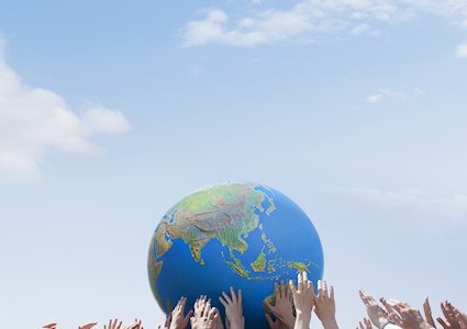 Hands hold up a ball that has the continents on it. 